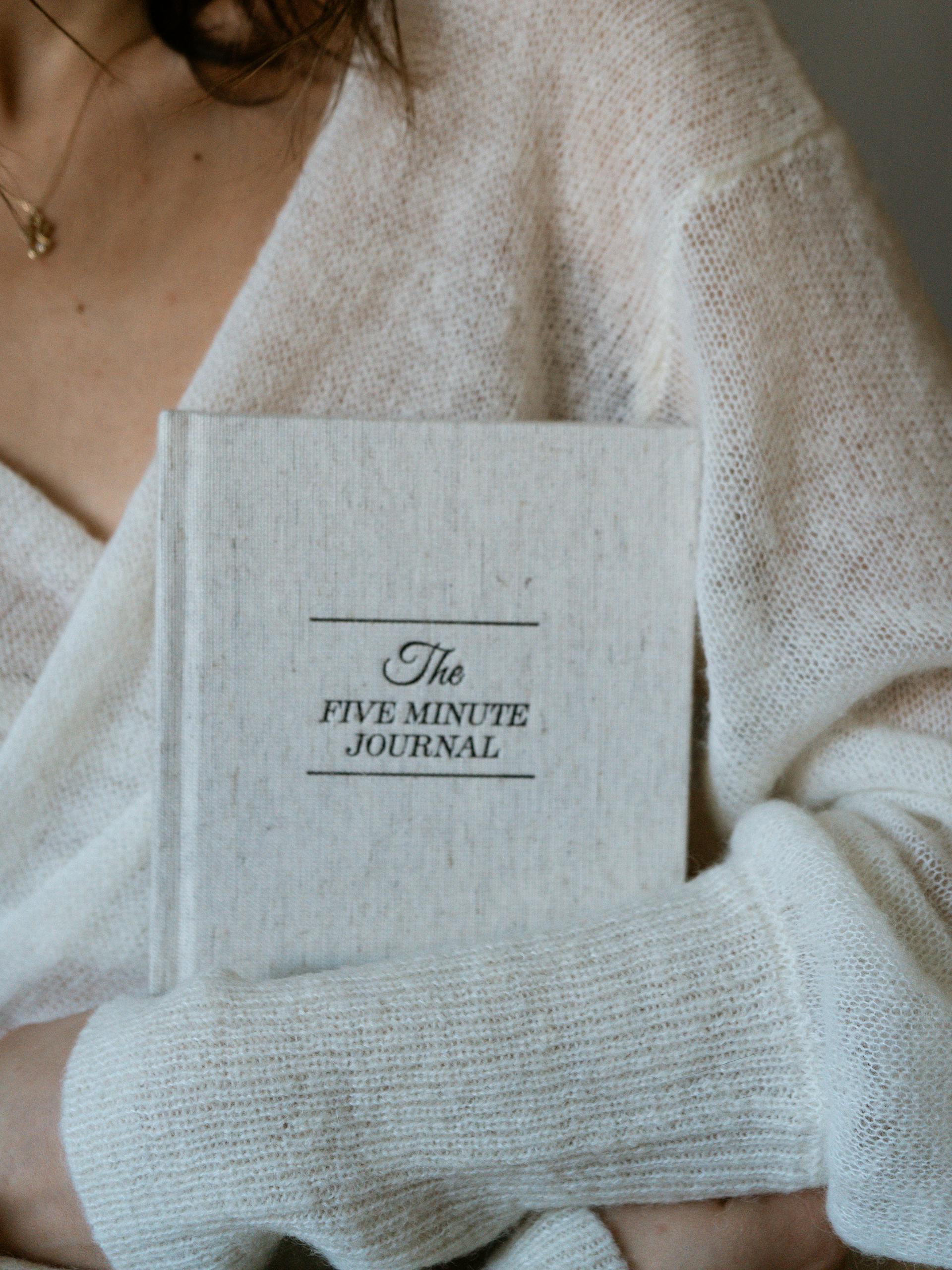 Close-up of a woman in a sweater holding The Five Minute Journal.