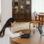 Two students using laptops and writing on paper in a cozy library, fostering collaborative learning.